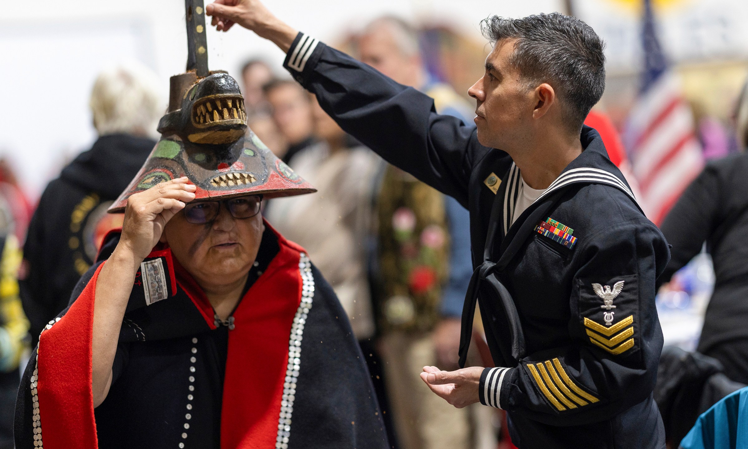 A member of the U.S. Navy sprinkles tobacco on top of a killer whale clan hat, which is considered to bring good fortune, during a Navy ceremony Saturday, Oct. 26, 2024, in Angoon, Alaska, to apologize for the 1882 military bombing of the Tlingit village in Angoon. (Nobu Koch/Sealaska Heritage Institute via AP)