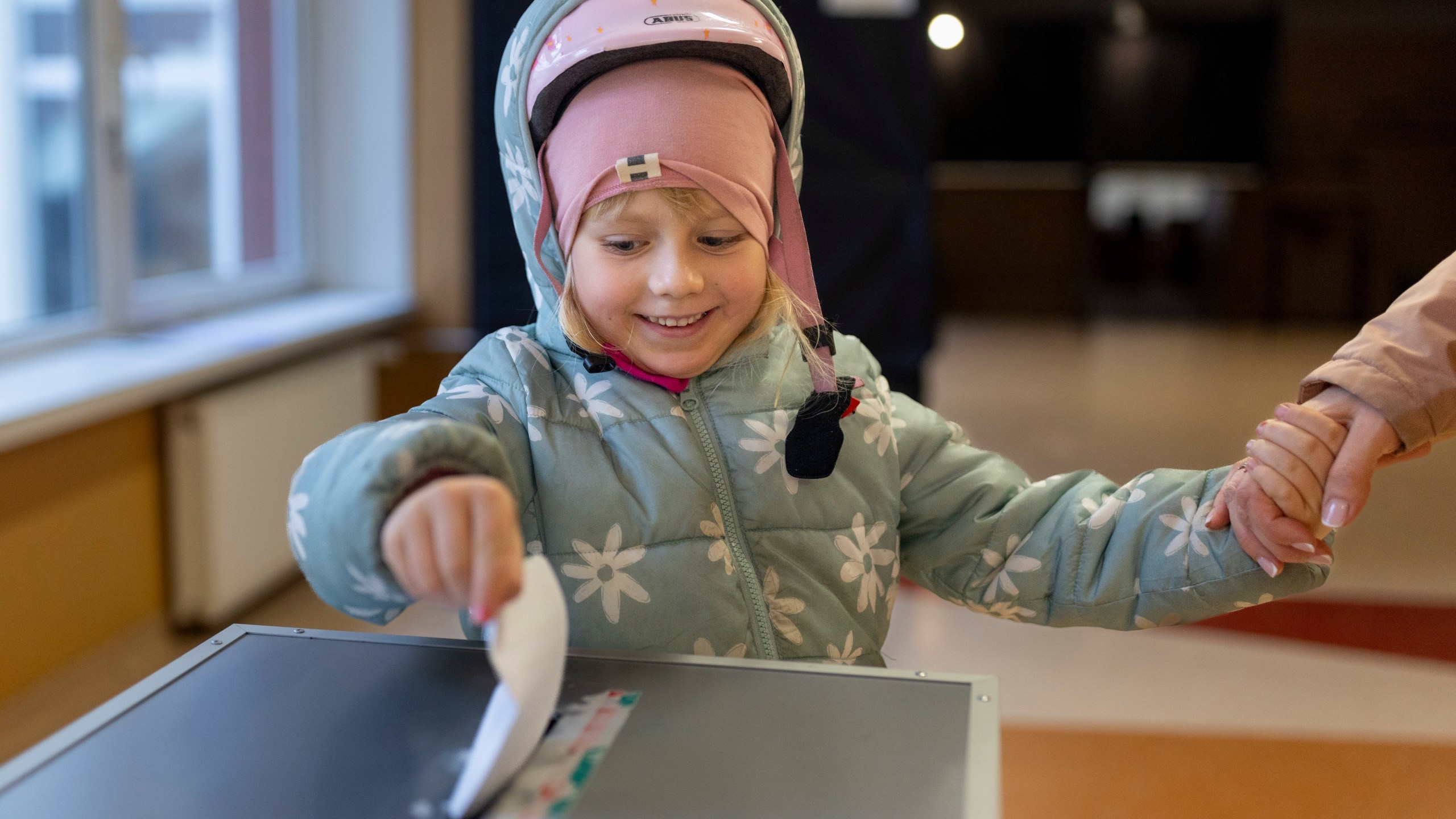 A girl helps to cast a ballot at a polling station during a second round of voting in parliamentary election, in Vilnius, Lithuania, Sunday, Oct. 27, 2024. (AP Photo/Mindaugas Kulbis)