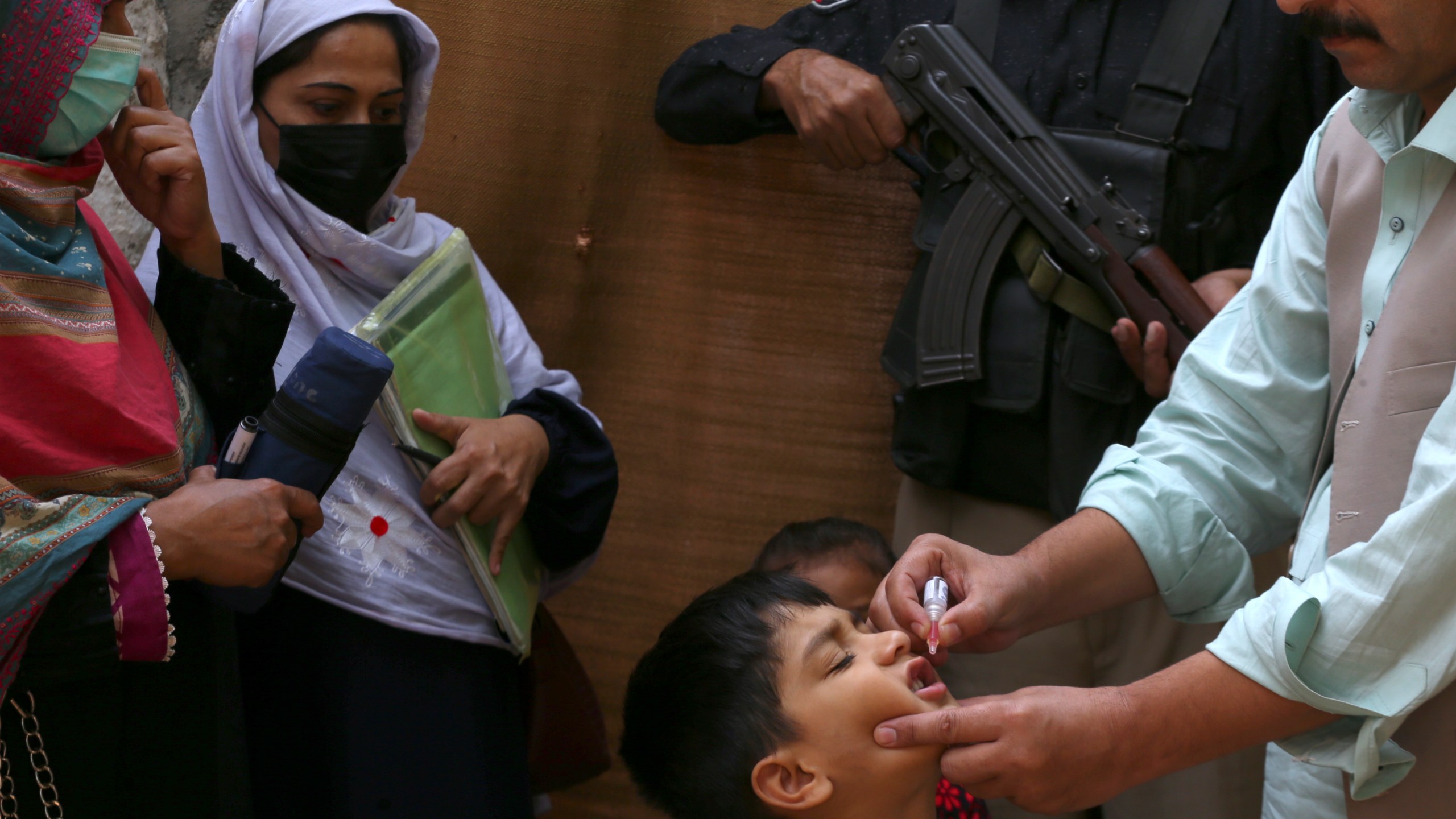 A police officer stands guard as a health worker, right, administers a polio vaccine to a child in a neighbourhood of Peshawar, Pakistan, Monday, Oct. 28, 2024. (AP Photo/Mohammad Sajjad)