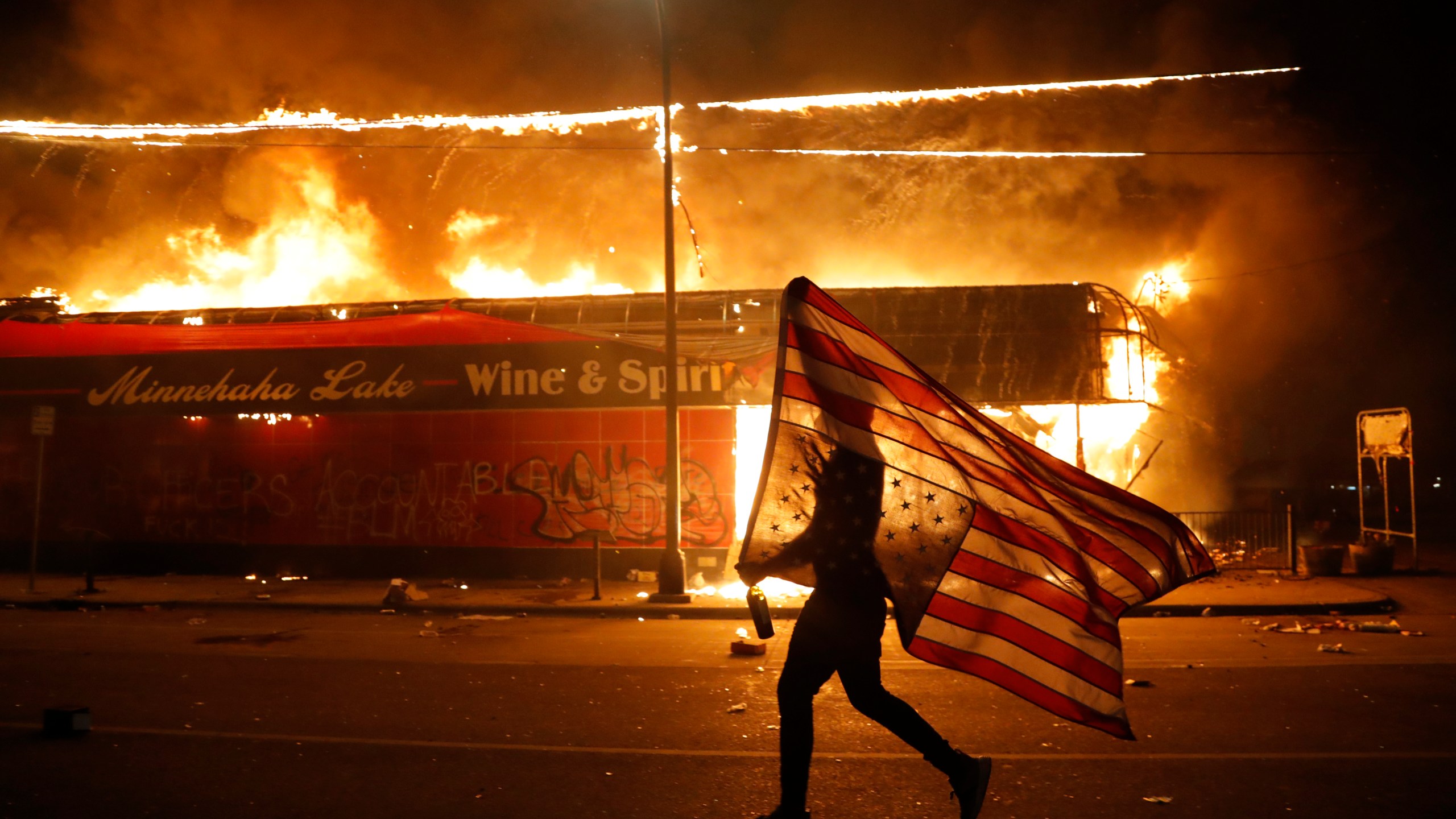 FILE - A protester carries a U.S. flag upside down, a sign of distress, next to a burning building on May 28, 2020, in Minneapolis. (AP Photo/Julio Cortez, File)