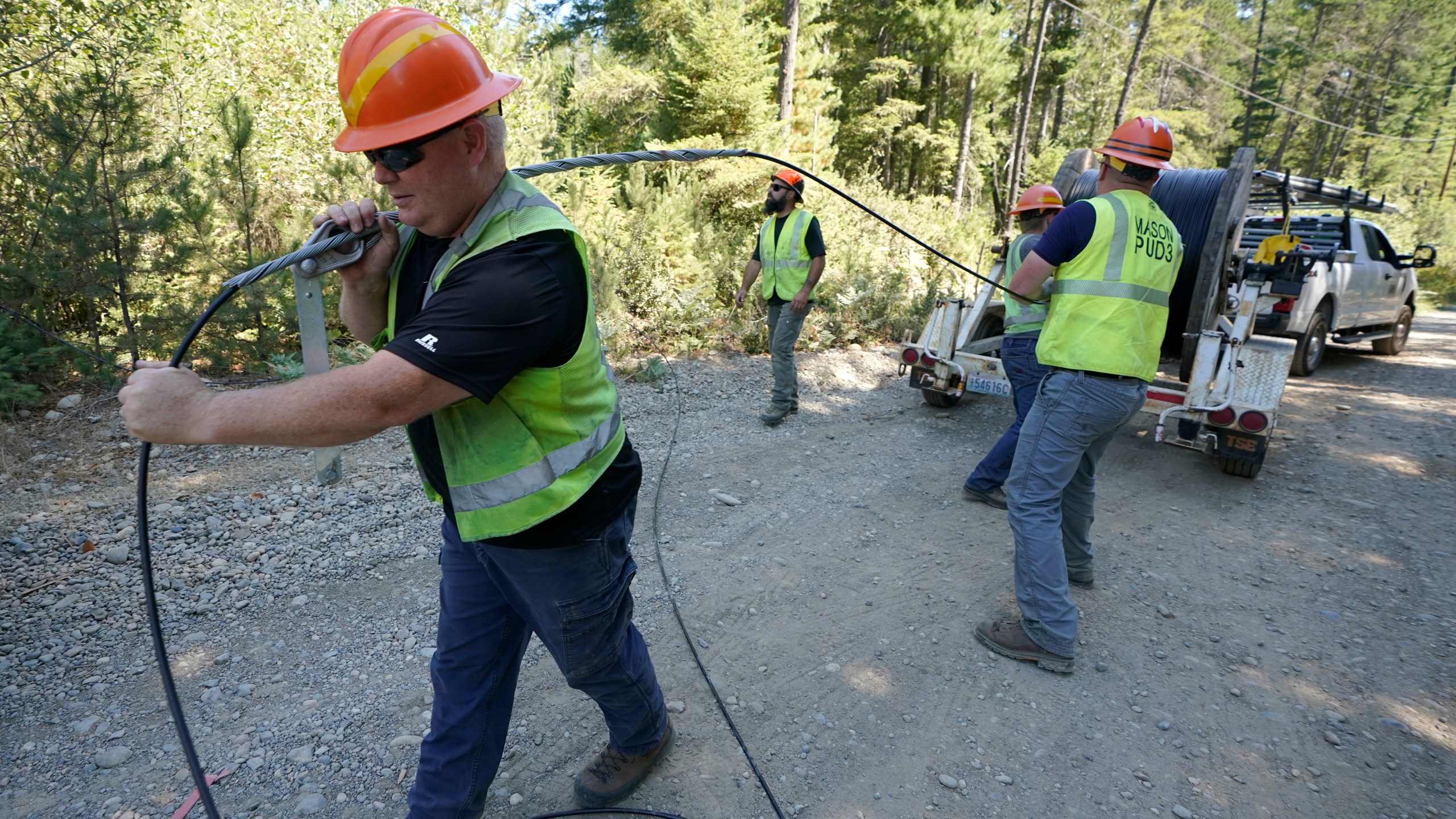 FILE - Carl Roath, left, a worker with the Mason County (Wash.) Public Utility District, pulls fiber optic cable on a project to install broadband internet service in the area surrounding Lake Christine near Belfair, Wash., on Aug. 4, 2021. (AP Photo/Ted S. Warren, File)