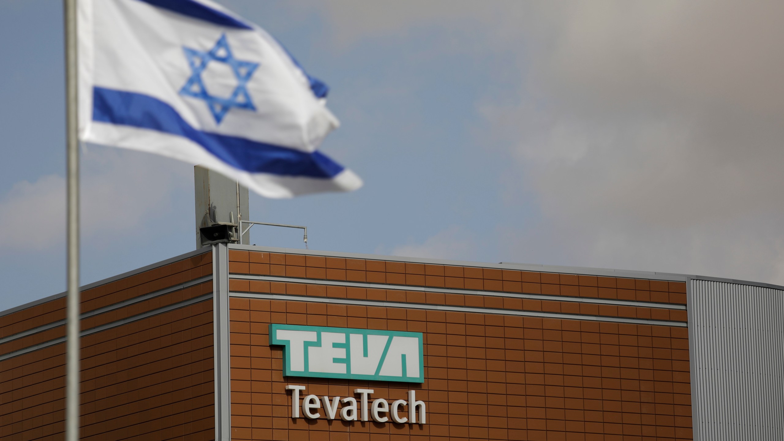 FILE - Israeli flag flies outside Teva Pharmaceutical facility building in Neot Hovav, Israel, on Dec. 14, 2017. (AP Photo/Tsafrir Abayov, File)