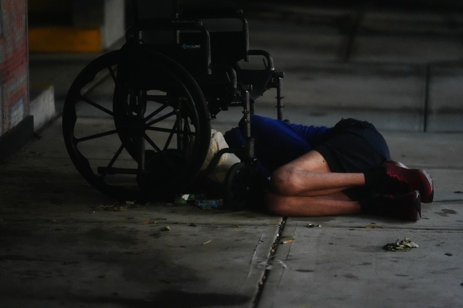 A homeless person sleeps under a wheelchair alongside a parking garage in deserted downtown Tampa, Fla., during the approach of Hurricane Milton, Wednesday, Oct. 9, 2024.