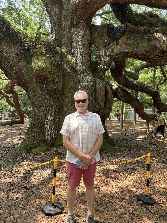 An older man in sunglasses in front of a tree.