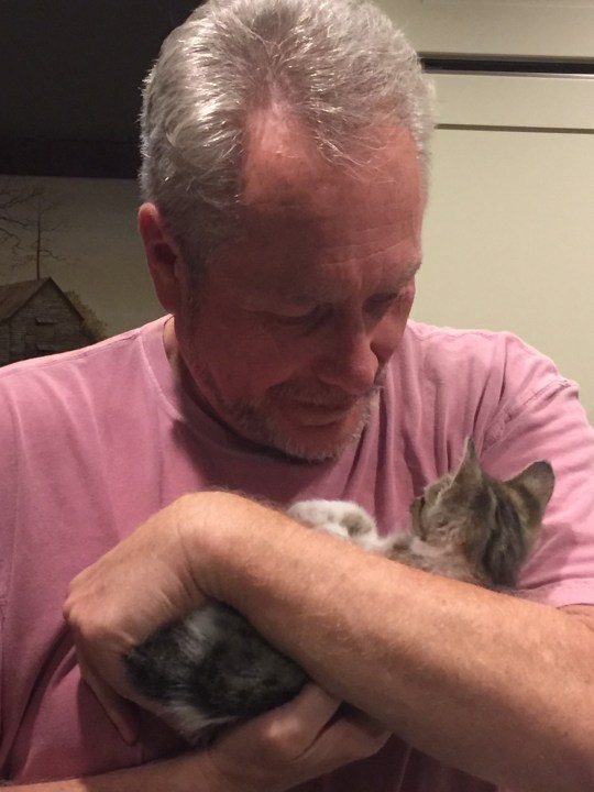 An older man hugging a kitten.