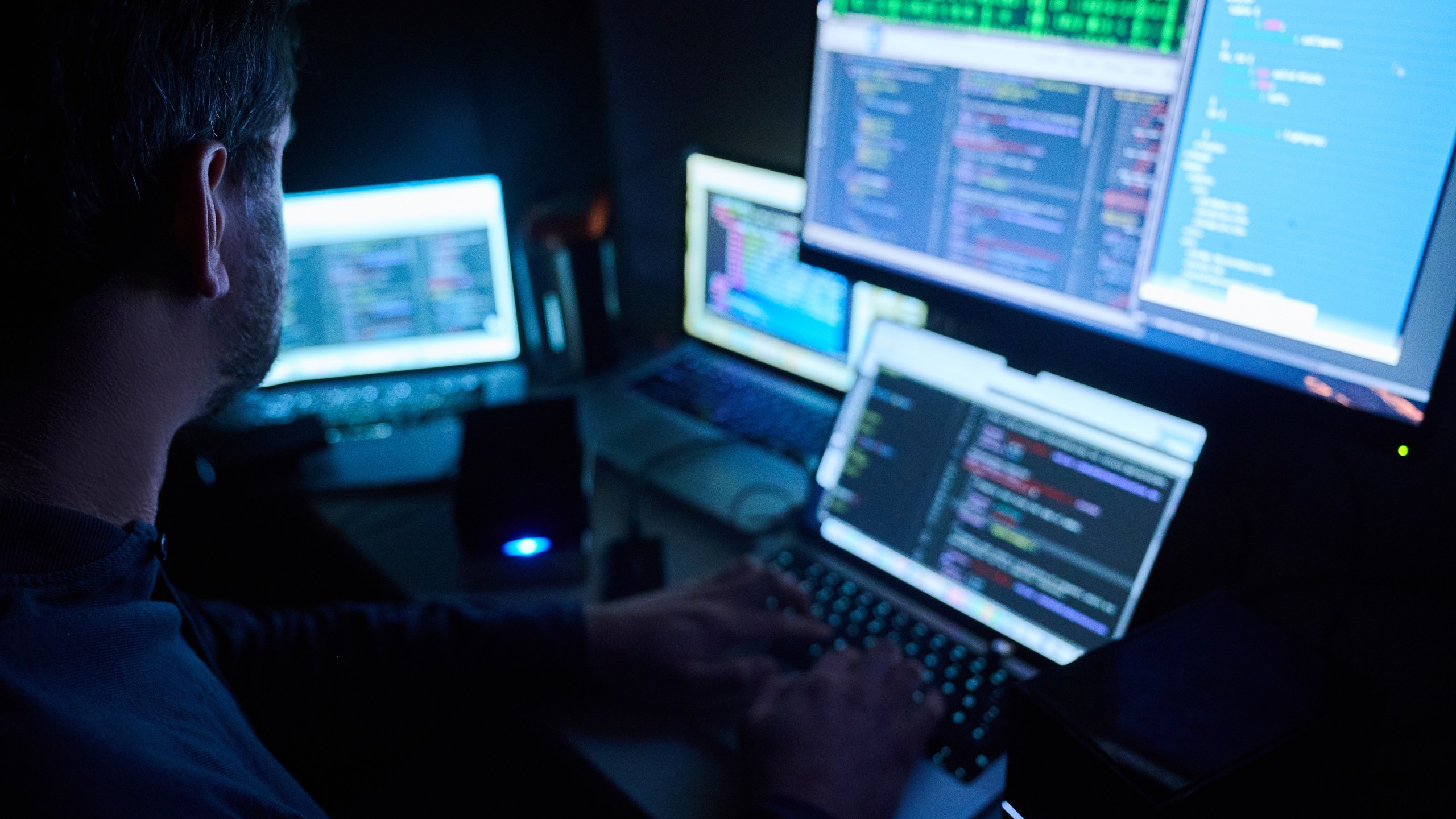 Fictitious html pages and hacker programs are seen on screens while a man has his hands on the keyboard.