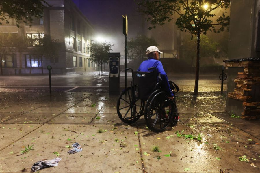 A woman in a wheelchair makes her way along a downtown sidewalk as Hurricane Milton makes landfall on October 09, 2024, in Tampa, Florida.