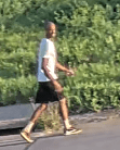 A black man in black shorts and white shirt walking.