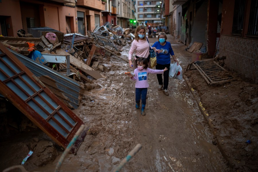 A child walks with her mother and grandmother through a street with piled furniture and rubbish on the sides, in an area affected by floods in Paiporta, Valencia, Spain, Tuesday, Nov. 5, 2024. (AP Photo/Emilio Morenatti)