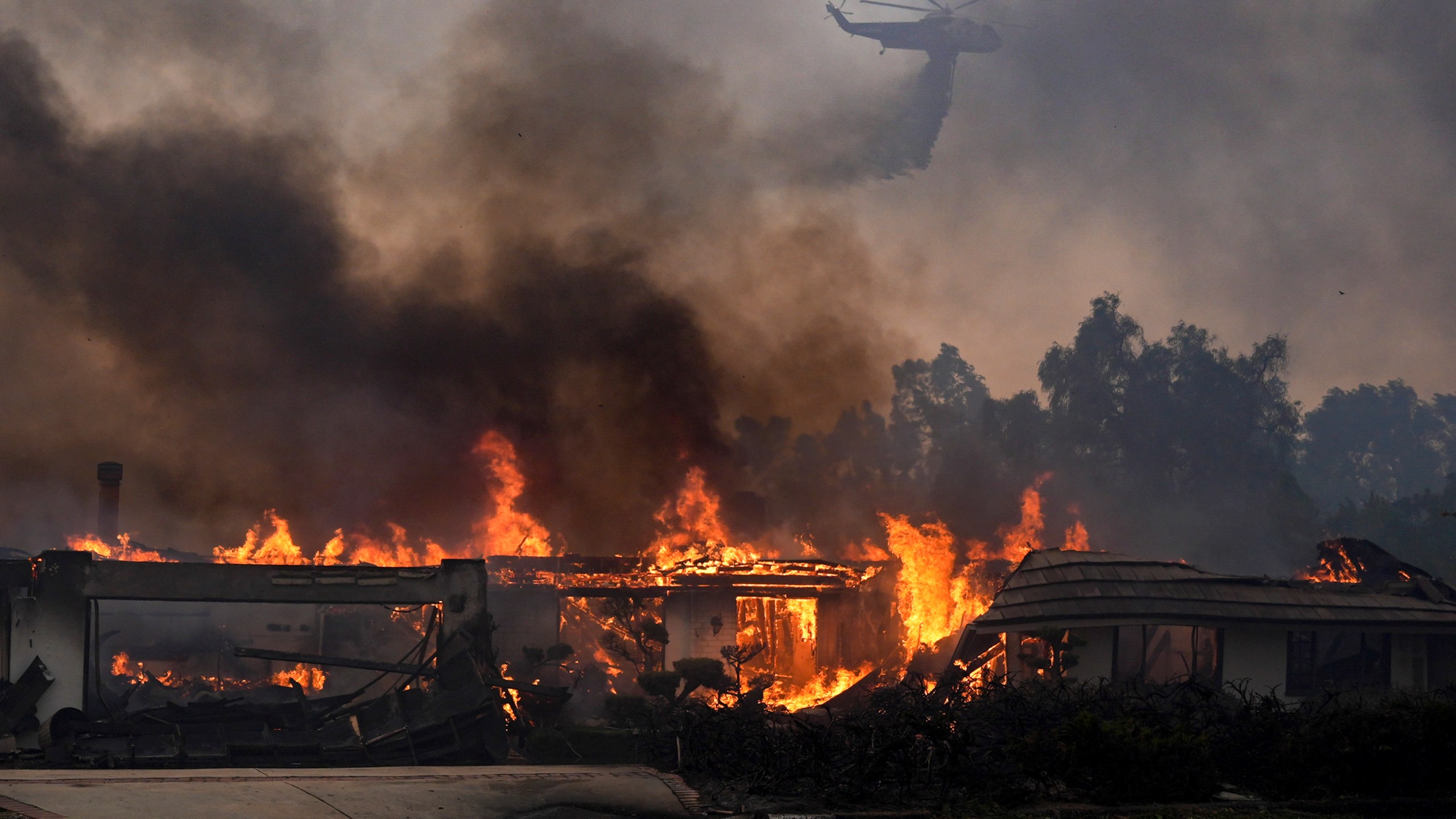 A helicopter drops water over a burning home in the Mountain fire, Wednesday, Nov. 6, 2024, near Camarillo, Calif. (AP Photo/Marcio Jose Sanchez)