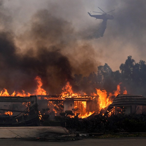 A helicopter drops water over a burning home in the Mountain fire, Wednesday, Nov. 6, 2024, near Camarillo, Calif. (AP Photo/Marcio Jose Sanchez)