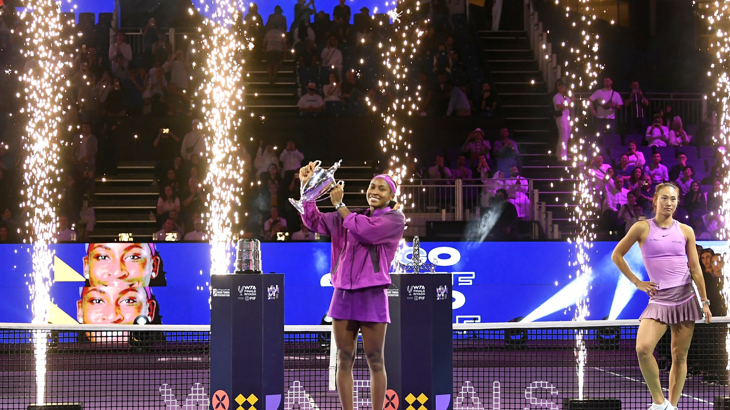 Coco Gauff of the U.S. holds her trophy next to China's Qinwen Zheng, after defeating her in their women's singles final match of the WTA finals at the King Saud University Indoor Arena, in Riyadh, Saudi Arabia, Saturday, Nov. 9, 2024. (AP Photo)