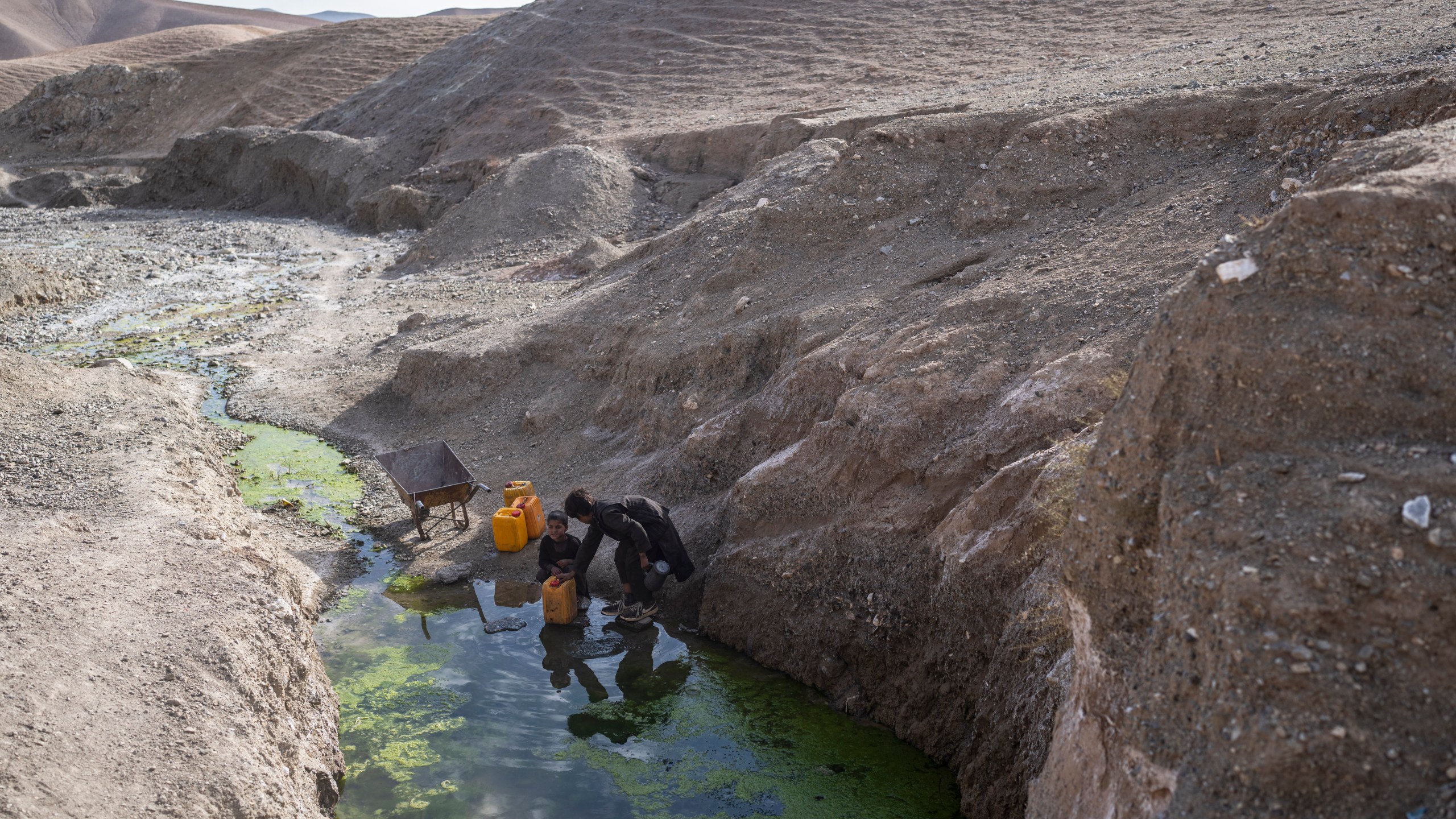 FILE -Two brothers fill canisters with water from a stagnant pool about 3 kilometers (2 miles) from their home in Kamar Kalagh village outside Herat, Afghanistan, Friday, Nov. 26, 2021. (AP Photo/Petros Giannakouris, File)