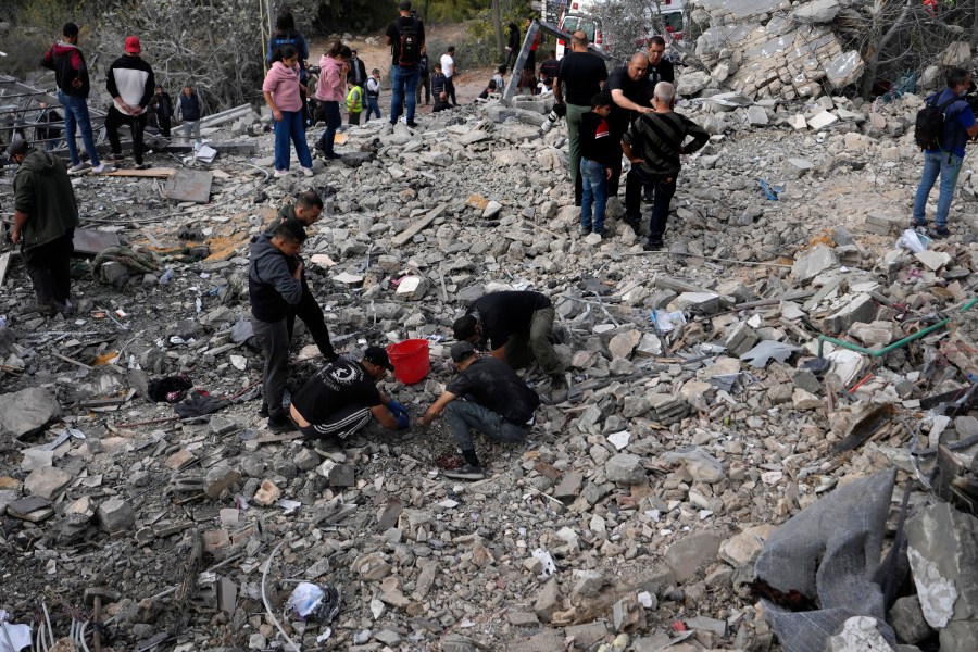 Rescue workers and people, centre, search for victims under the rubble of a destroyed house hit in an Israeli airstrike, in Aalmat village, northern Lebanon, Sunday, Nov. 10, 2024. (AP Photo/Hassan Ammar)