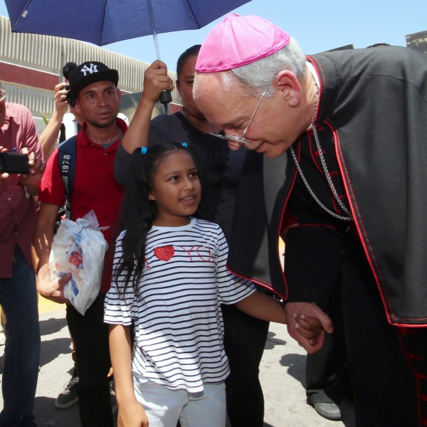 FILE - El Paso Catholic Bishop Mark Seitz talks with Celsia Palma, 9, of Honduras, as they walk to the Paso Del Norte International Port of Entry, Thursday, June, 27, 2019, in Juarez, Mexico. (AP Photo/Rudy Gutierrez, File)