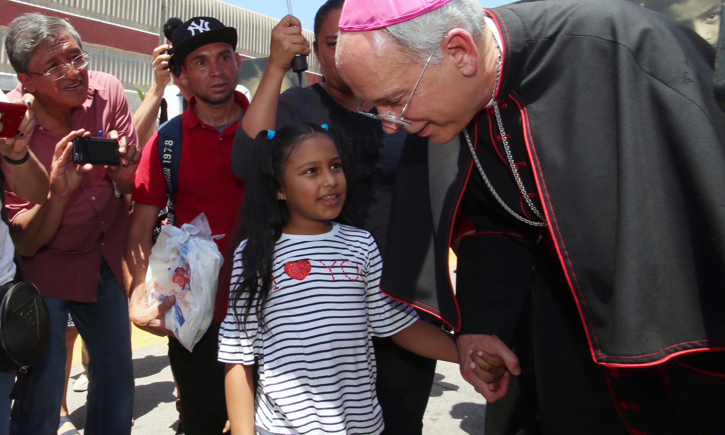 FILE - El Paso Catholic Bishop Mark Seitz talks with Celsia Palma, 9, of Honduras, as they walk to the Paso Del Norte International Port of Entry, Thursday, June, 27, 2019, in Juarez, Mexico. (AP Photo/Rudy Gutierrez, File)