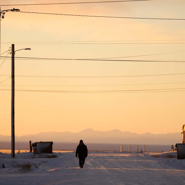 A resident walks up a street as the sun rises Tuesday, Oct. 15, 2024, in Kaktovik, Alaska. (AP Photo/Lindsey Wasson)