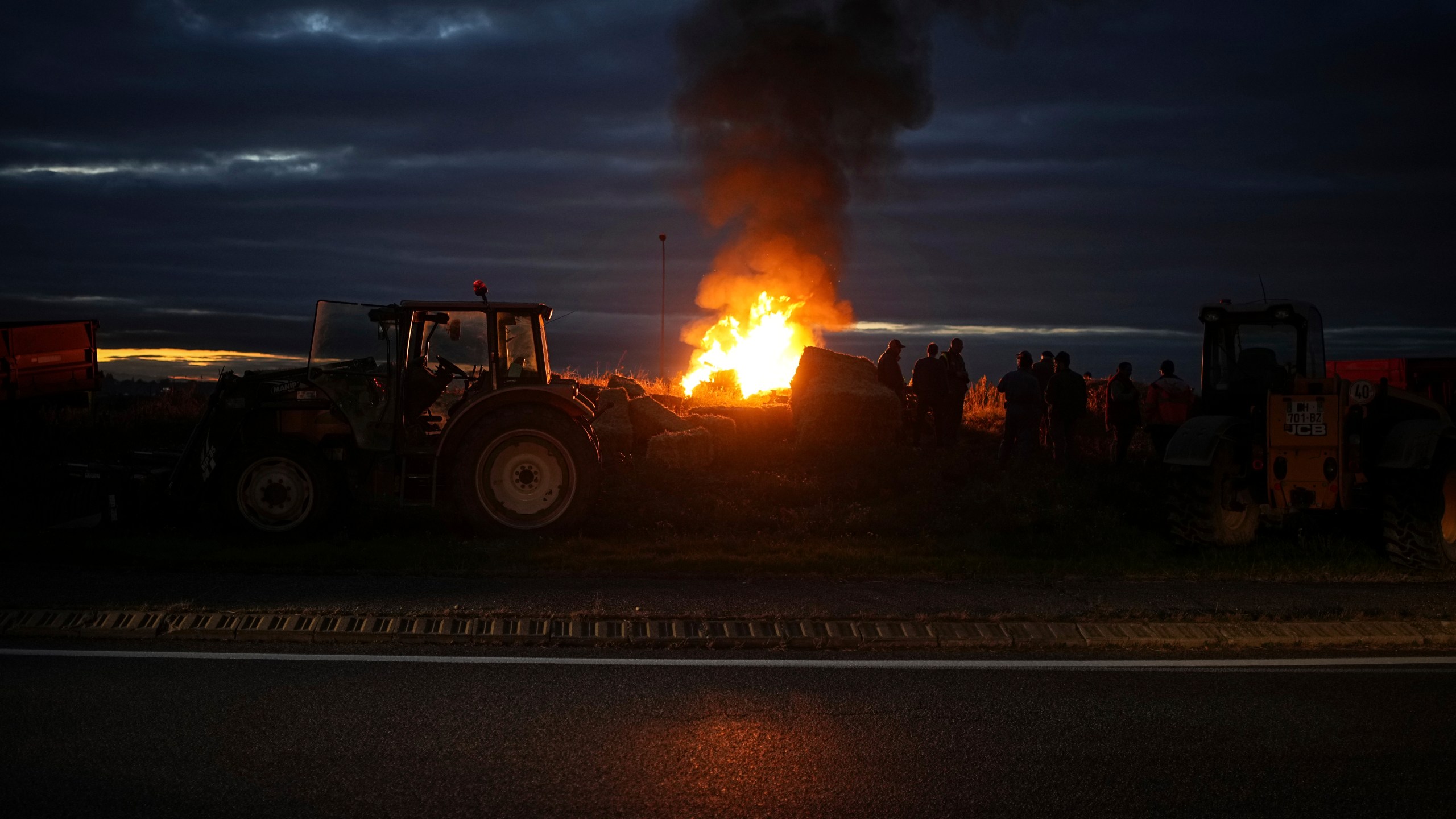 Farmers gather around a fire to protest against the EU-Mercosur trade agreement, in Saint-Laurent-de-Mure, near Lyon, central France, Monday, Nov. 18, 2024. (AP Photo/Laurent Cipriani)