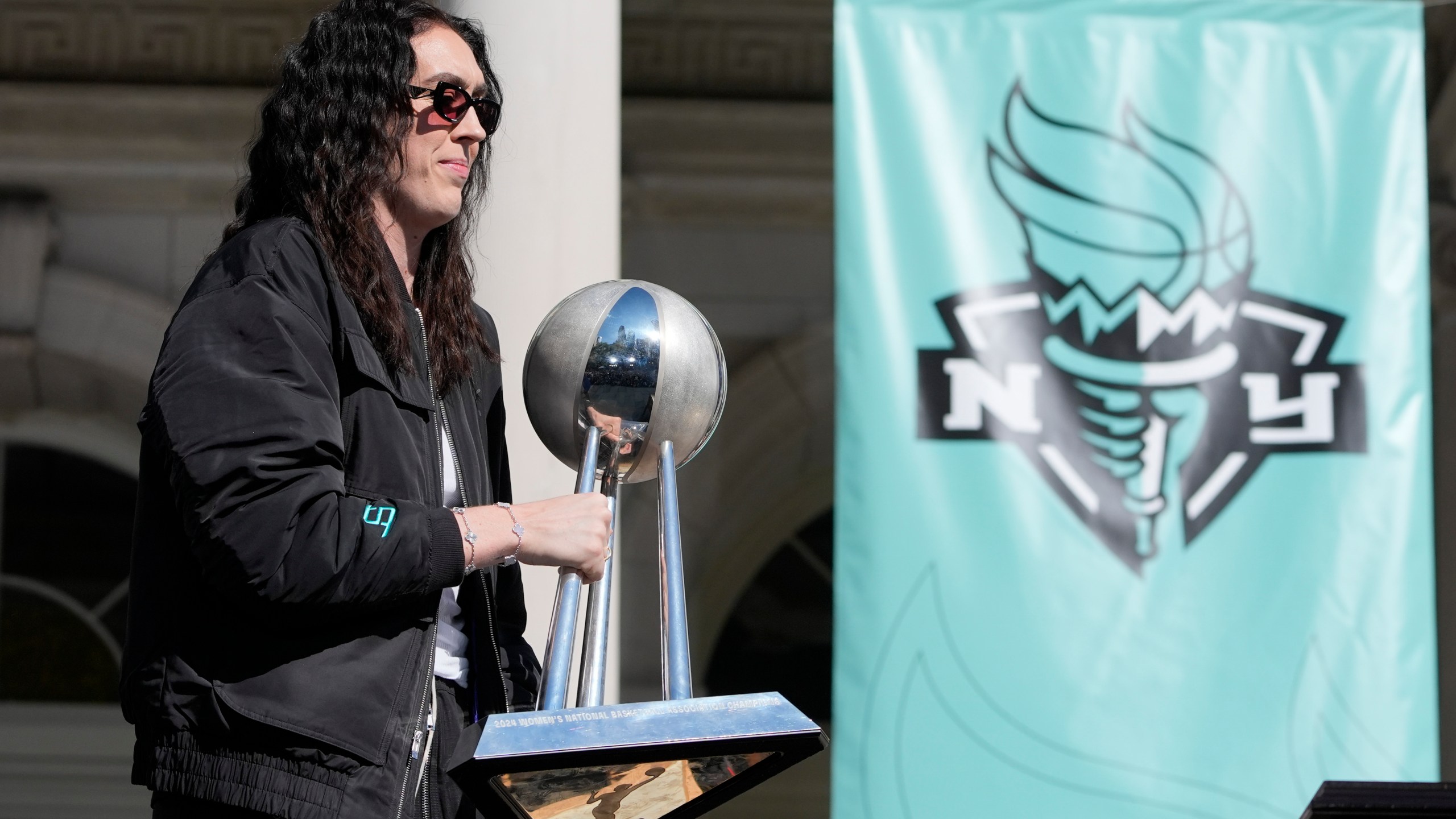 New York Liberty Breanna Stewart places the championship trophy on a table as she arrives on stage during a ceremony after a parade in honor of the Liberty's WNBA basketball championship at City Hall in New York, Thursday, Oct. 24, 2024. (AP Photo/Seth Wenig)