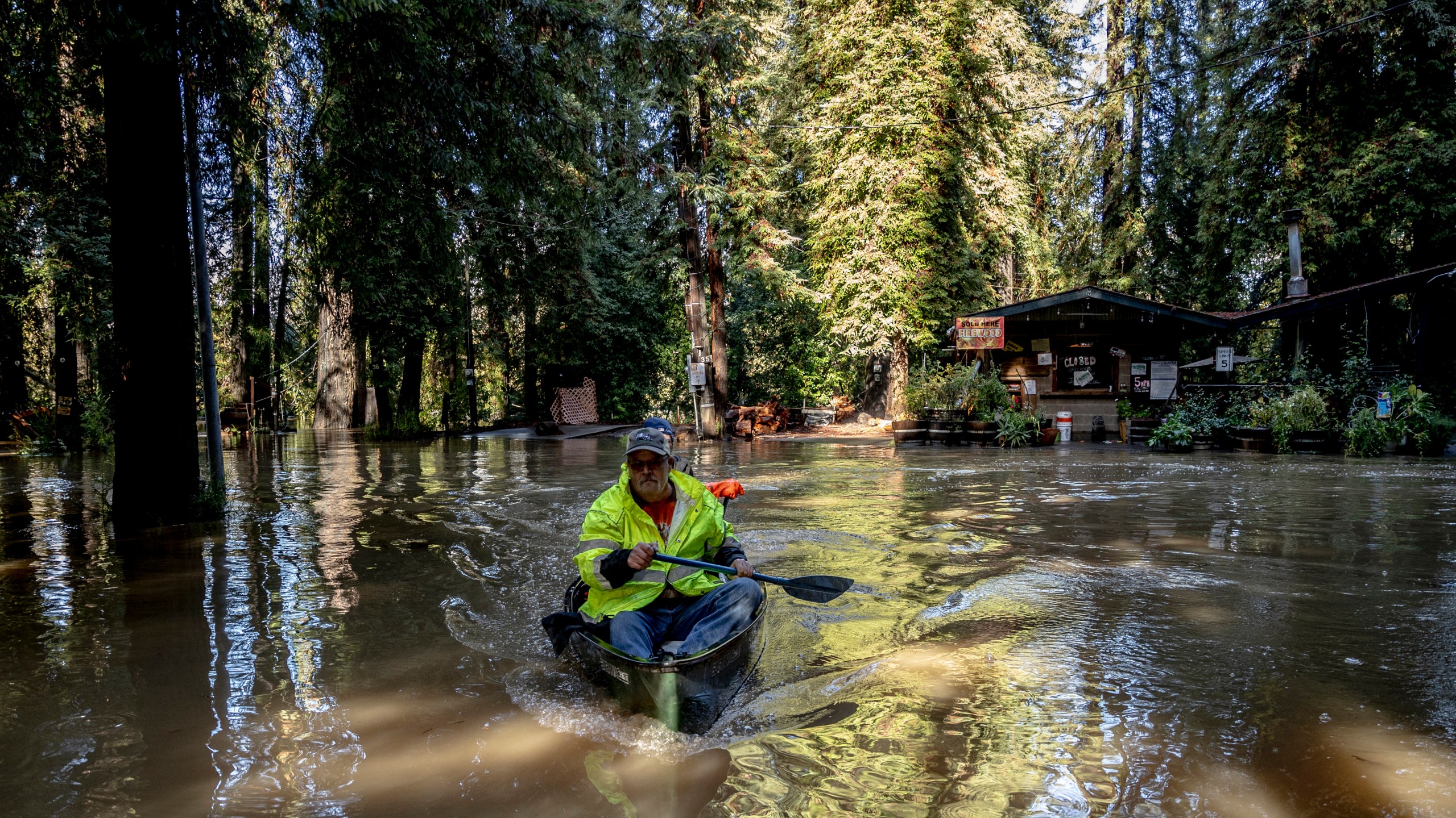 John Phillips, front, and neighbor Kevin Ozorkiewicz row a canoe at the flooded Mirabel RV Park & Campground after a major storm in Forestville, Calif., Saturday, Nov. 23, 2024. (Stephen Lam/San Francisco Chronicle via AP)