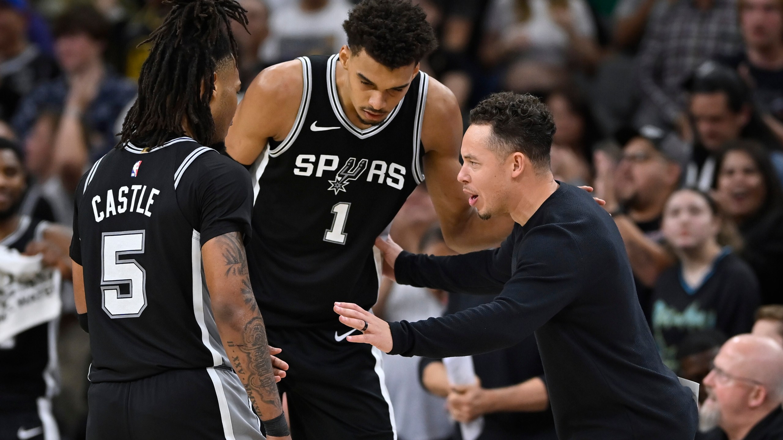 San Antonio Spurs acting head coach Mitch Johnson, right, speaks with Spurs players Victor Wembanyama (1) and Stephon Castle (5) during the second half of their NBA basketball game against the Golden State Warriors, Saturday, Nov. 23, 2024, in San Antonio. (AP Photo/Darren Abate)