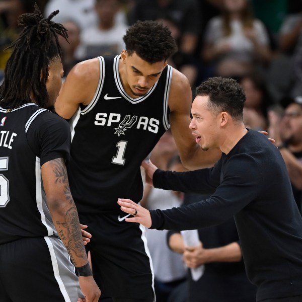 San Antonio Spurs acting head coach Mitch Johnson, right, speaks with Spurs players Victor Wembanyama (1) and Stephon Castle (5) during the second half of their NBA basketball game against the Golden State Warriors, Saturday, Nov. 23, 2024, in San Antonio. (AP Photo/Darren Abate)