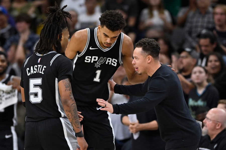 San Antonio Spurs acting head coach Mitch Johnson, right, speaks with Spurs players Victor Wembanyama (1) and Stephon Castle (5) during the second half of their NBA basketball game against the Golden State Warriors, Saturday, Nov. 23, 2024, in San Antonio. (AP Photo/Darren Abate)