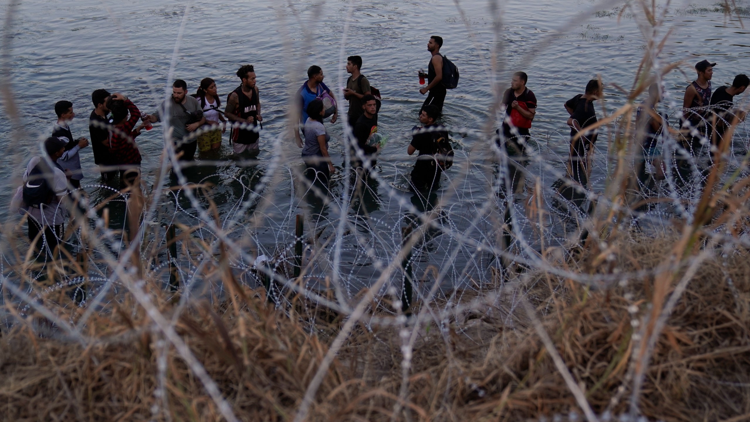 FILE - Migrants wait to climb over concertina wire after they crossed the Rio Grande and entered the U.S. from Mexico, Sept. 23, 2023, in Eagle Pass, Texas. (AP Photo/Eric Gay, File)