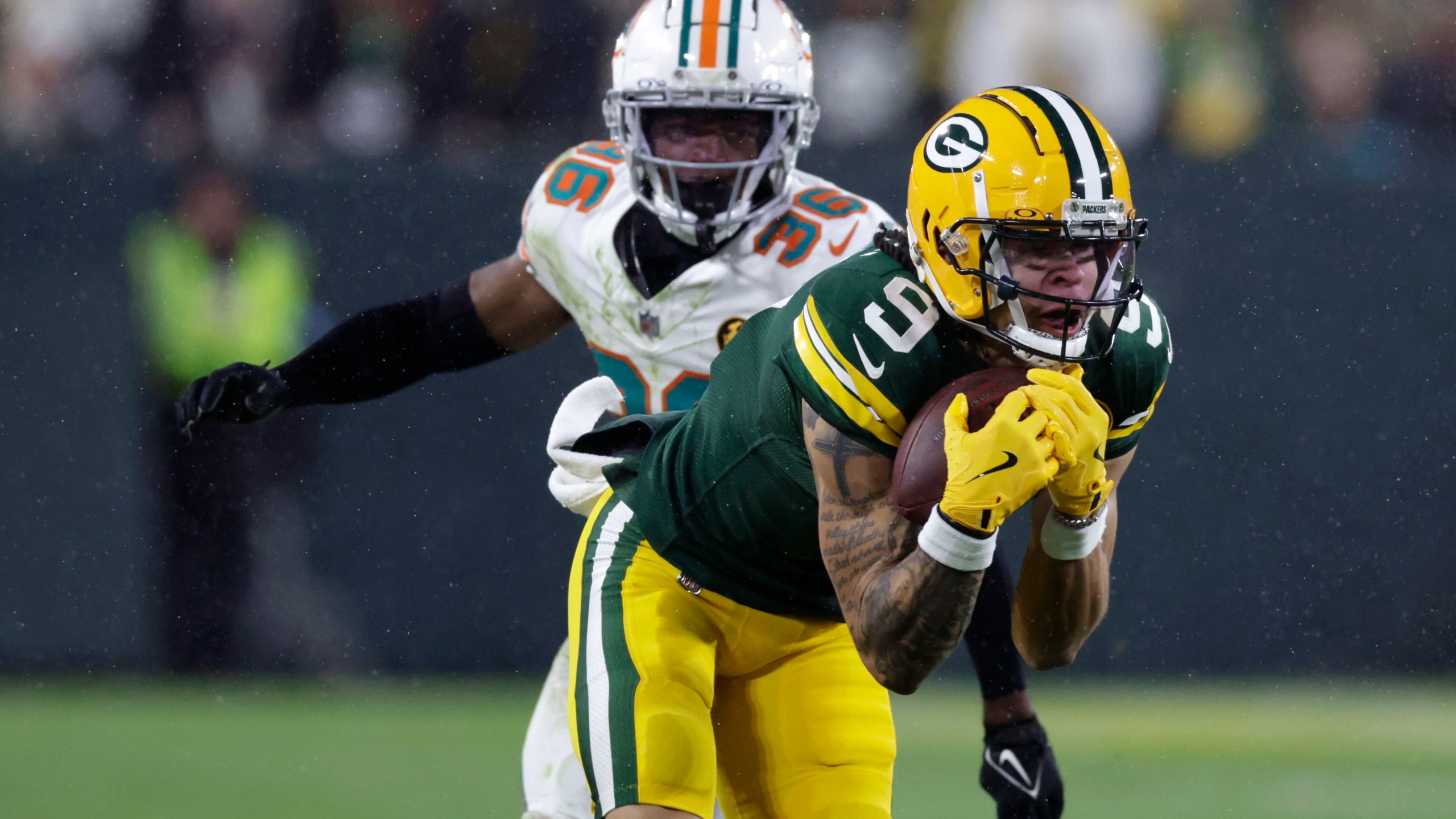 Green Bay Packers wide receiver Christian Watson (9) catches a pass ahead of Miami Dolphins cornerback Storm Duck (36) during the second half of an NFL football game Thursday, Nov. 28, 2024, in Green Bay, Wis. (AP Photo/Matt Ludtke)