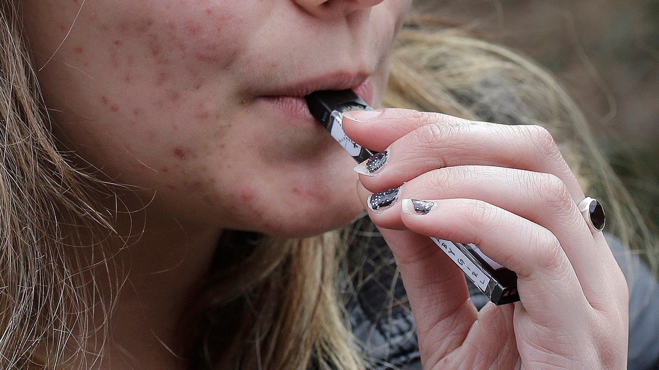 FILE - A high school student uses a vaping device near a school campus in Cambridge, Mass., April 11, 2018. (AP Photo/Steven Senne, File)