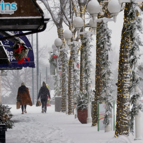 Shoppers walk through blowing and drifting snow, Monday, Dec. 2, 2024, in downtown St. Joseph, Mich. (Don Campbell/The Herald-Palladium via AP)