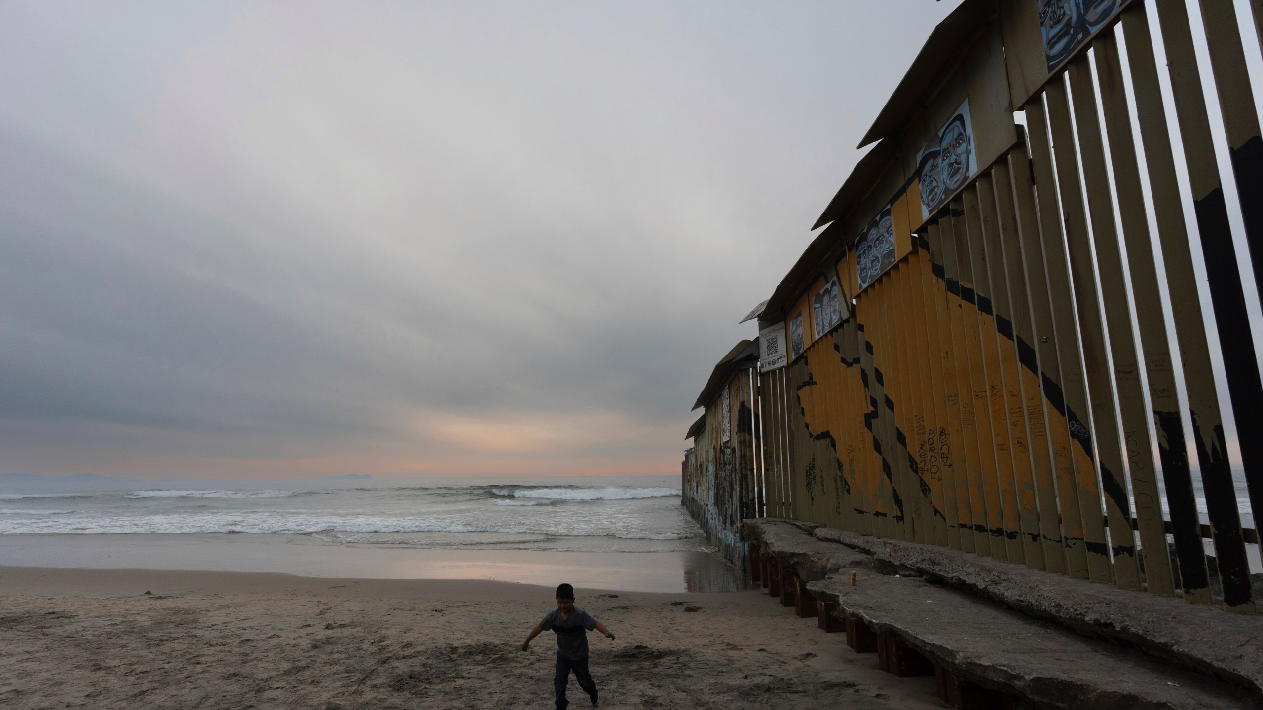 A boy walks near where a border wall separating the United States from Mexico reaches the Pacific Ocean, Tuesday, Nov. 26, 2024, in Tijuana, Mexico. (AP Photo/Gregory Bull)