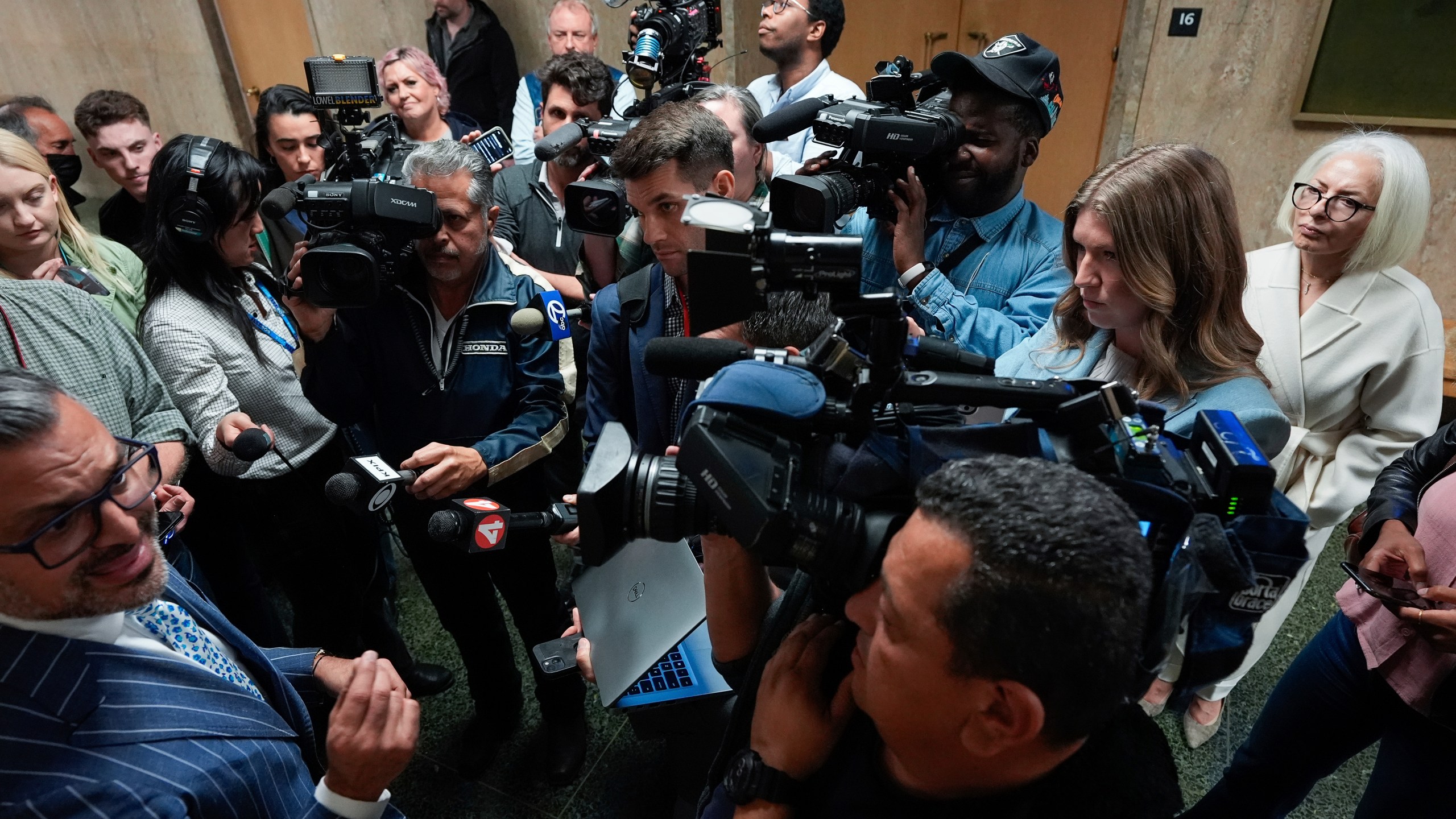 Mahnaz Tayarani, right, in white coat, mother of Nima Momeni, who is charged with murder in Cash App founder Bob Lee's stabbing death, watches as defense attorney Saam Zangeneh, bottom left, speaks to reporters after exiting the courtroom at the Hall of Justice for Momeni's murder trial Tuesday, Dec. 3, 2024, in San Francisco. (AP Photo/Godofredo A. Vásquez)