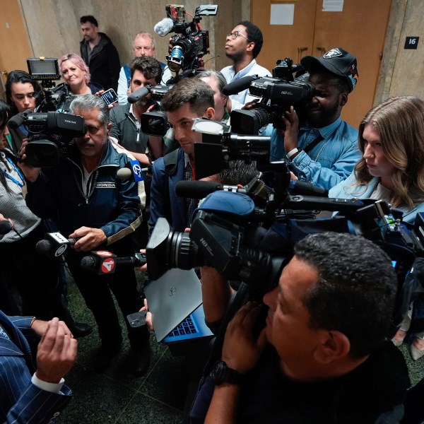 Mahnaz Tayarani, right, in white coat, mother of Nima Momeni, who is charged with murder in Cash App founder Bob Lee's stabbing death, watches as defense attorney Saam Zangeneh, bottom left, speaks to reporters after exiting the courtroom at the Hall of Justice for Momeni's murder trial Tuesday, Dec. 3, 2024, in San Francisco. (AP Photo/Godofredo A. Vásquez)