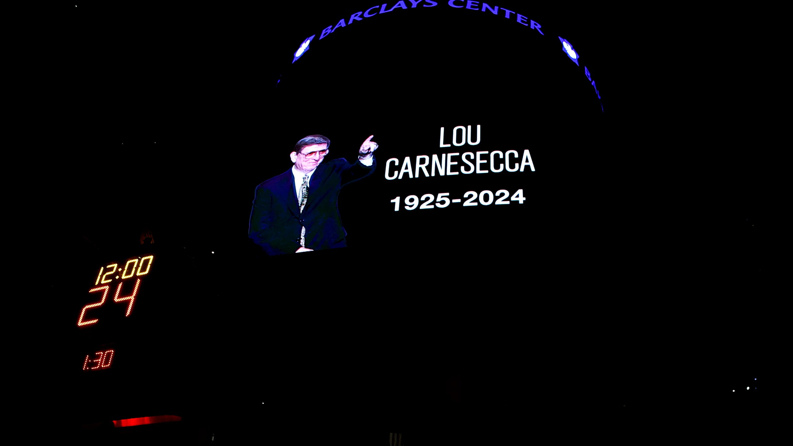 Fans pause for a moment of silence in memory of former St. John's men's basketball coach Lou Carnesecca before an NBA basketball game between the Orlando Magic and the Brooklyn Nets, Sunday, Dec. 1, 2024, in New York. (AP Photo/Noah K. Murray)