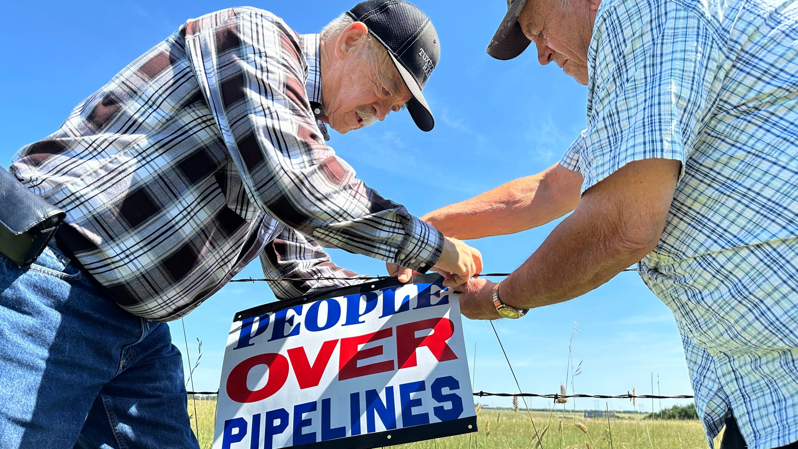 FILE - Gaylen Dewing, left, and Marvin Abraham affix a sign to a roadside fence east of Bismarck, N.D., Tuesday, Aug. 15, 2023, in opposition to Summit Carbon Solutions' proposed five-state, 2,000-mile pipeline network to carry carbon dioxide emissions from dozens of Midwestern ethanol plants to North Dakota for permanent storage deep underground. (AP Photo/Jack Dura, File)