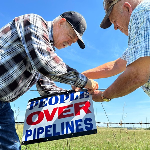 FILE - Gaylen Dewing, left, and Marvin Abraham affix a sign to a roadside fence east of Bismarck, N.D., Tuesday, Aug. 15, 2023, in opposition to Summit Carbon Solutions' proposed five-state, 2,000-mile pipeline network to carry carbon dioxide emissions from dozens of Midwestern ethanol plants to North Dakota for permanent storage deep underground. (AP Photo/Jack Dura, File)