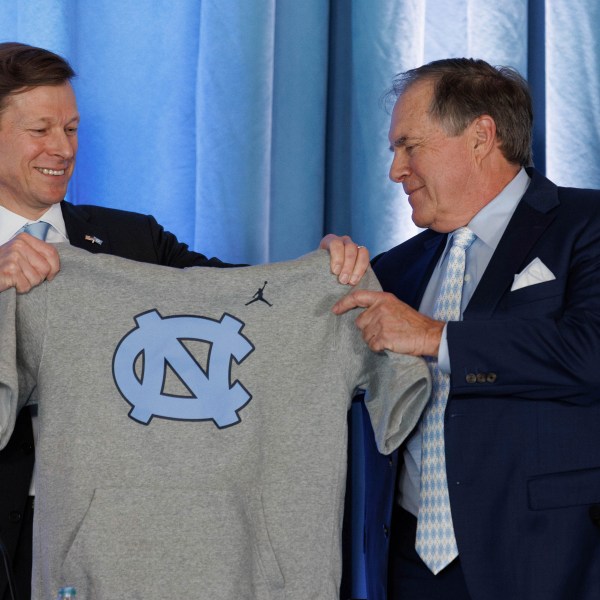 University of North Carolina Chancellor Lee Roberts, left, hands. new North Carolina coach Bill Belichick, right, a sleeveless UNC hoodie during an NCAA college football press conference in Chapel Hill, N.C., Thursday, Dec. 12, 2024. (AP Photo/Ben McKeown)