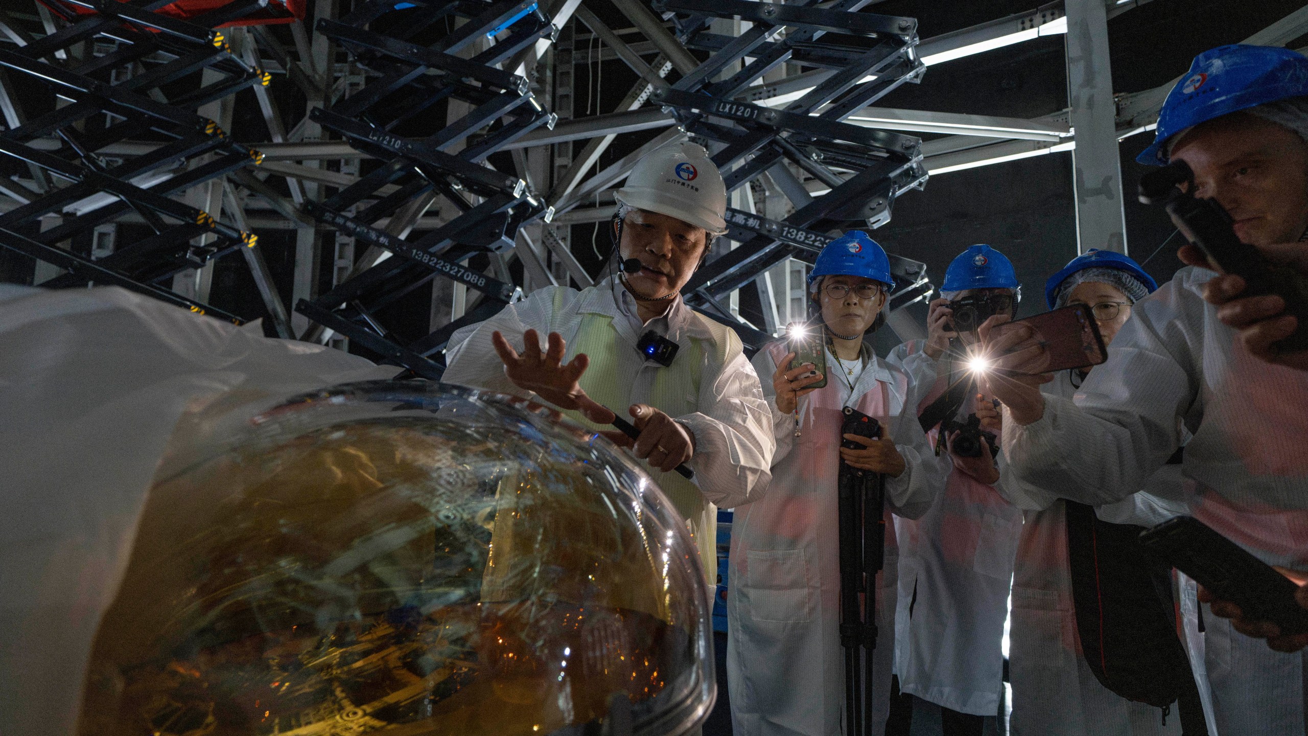 Wang Yifang, chief scientist and project manager at the Jiangmen Underground Neutrino Observatory briefs visitors on a Photomultiplier Tube used to convert photons into electrical signal, of which 20,000 pieces are used in the cosmic detector located 2297 feet (700 meters) underground in Kaiping, southern China's Guangdong province on Friday, Oct. 11, 2024. (AP Photo/Ng Han Guan)