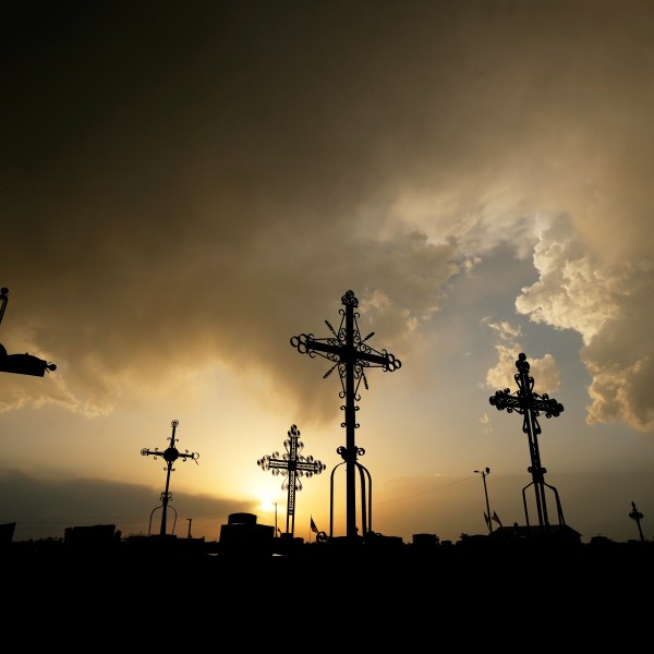 FILE - Iron crosses marking graves are silhouetted against storm clouds building over a cemetery Saturday, May 25, 2024, in Victoria, Kan. (AP Photo/Charlie Riedel, File)