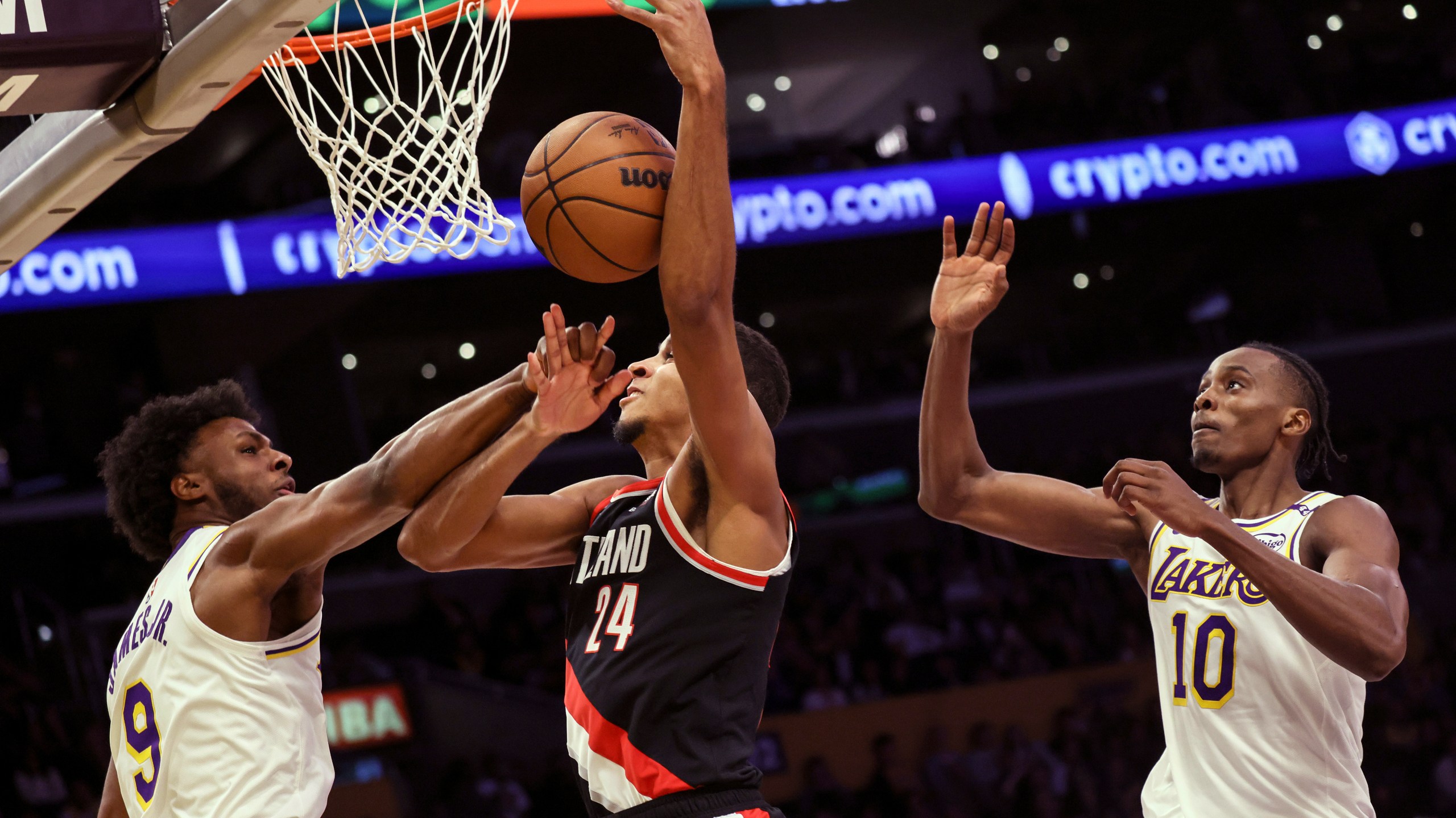 Los Angeles Lakers guard Bronny James, left, intercepts Portland Trail Blazers' forward Kris Murray, center, as he tries to score, next to Los Angeles Lakers center Christian Koloko during the second half of an NBA basketball game, Sunday, Dec. 8, 2024, in Los Angeles. (AP Photo/Etienne Laurent)