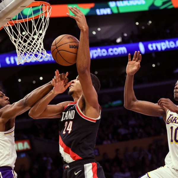 Los Angeles Lakers guard Bronny James, left, intercepts Portland Trail Blazers' forward Kris Murray, center, as he tries to score, next to Los Angeles Lakers center Christian Koloko during the second half of an NBA basketball game, Sunday, Dec. 8, 2024, in Los Angeles. (AP Photo/Etienne Laurent)