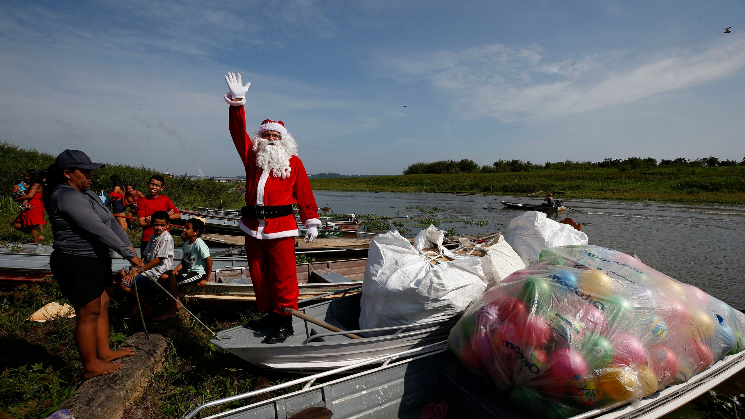 Jorge Barroso, dressed as Santa Claus, waves as he arrives on a boat to distribute Christmas gifts to children who live in the riverside communities of the Amazon, in Iranduba, Brazil, Saturday, Dec. 21, 2024. (AP Photo/Edmar Barros)