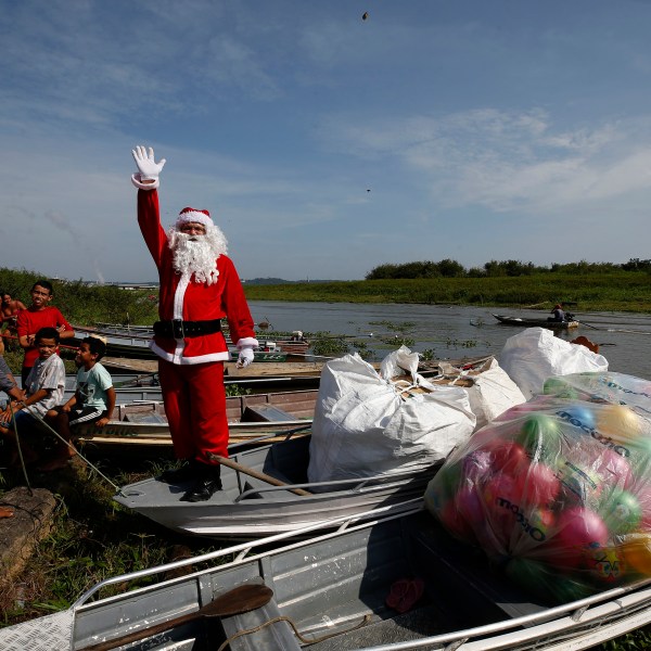 Jorge Barroso, dressed as Santa Claus, waves as he arrives on a boat to distribute Christmas gifts to children who live in the riverside communities of the Amazon, in Iranduba, Brazil, Saturday, Dec. 21, 2024. (AP Photo/Edmar Barros)