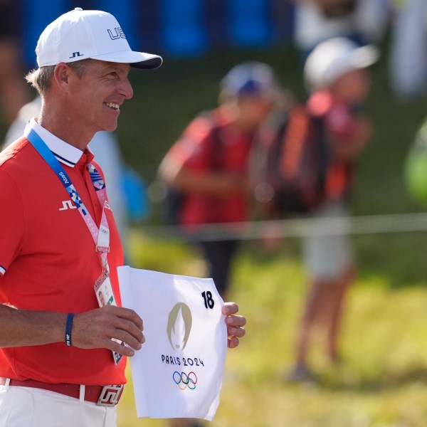 FILE - Ted Scott caddie for gold medalist Scottie Scheffler, of the United States, poses with the 18th hole flag after the end of the men's golf at the 2024 Summer Olympics, Sunday, Aug. 4, 2024, at Le Golf National in Saint-Quentin-en-Yvelines, France. (AP Photo/George Walker IV, File)