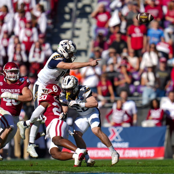 Navy quarterback Blake Horvath, top left, takes a hit from Oklahoma linebacker Lewis Carter (20) while attempting a pass during the first half of the Armed Forces Bowl NCAA college football game, Friday, Dec. 27, 2024, in Fort Worth, Texas. (AP Photo/Julio Cortez)