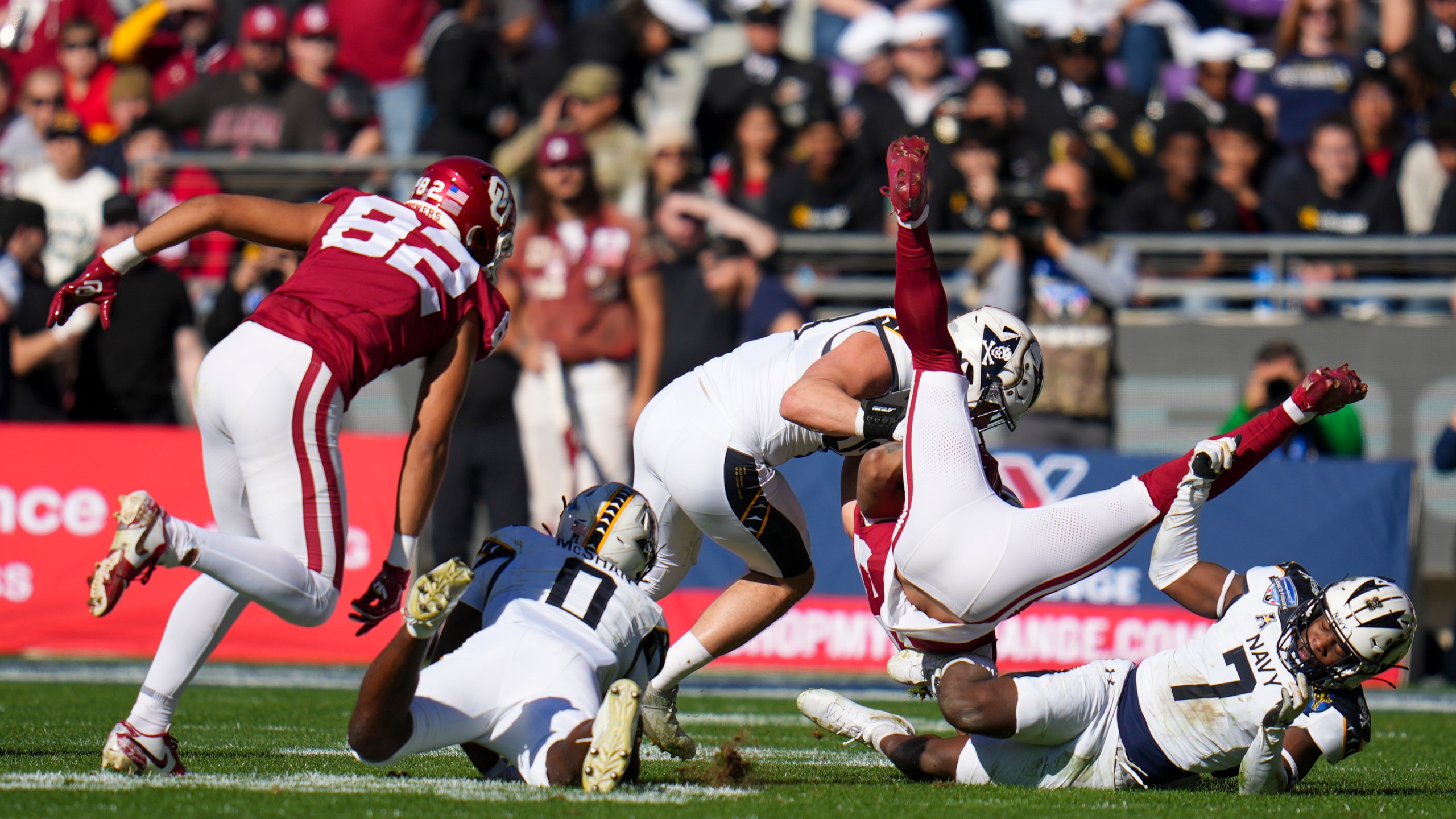 Oklahoma running back Gavin Sawchuk, second from right, is upended by Navy linebacker Mbiti Williams Jr. (7) and linebacker Kyle Jacob, center, during the first half of the Armed Forces Bowl NCAA college football game, Friday, Dec. 27, 2024, in Fort Worth, Texas. (AP Photo/Julio Cortez)