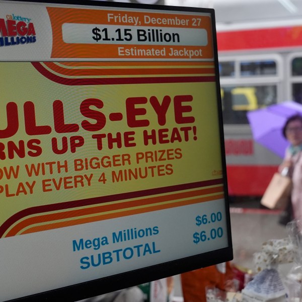 A pedestrian walks behind a sign advertising the estimated $1.15 billion Mega Millions jackpot at Rossi's Deli in San Francisco, Thursday, Dec. 26, 2024. (AP Photo/Jeff Chiu)