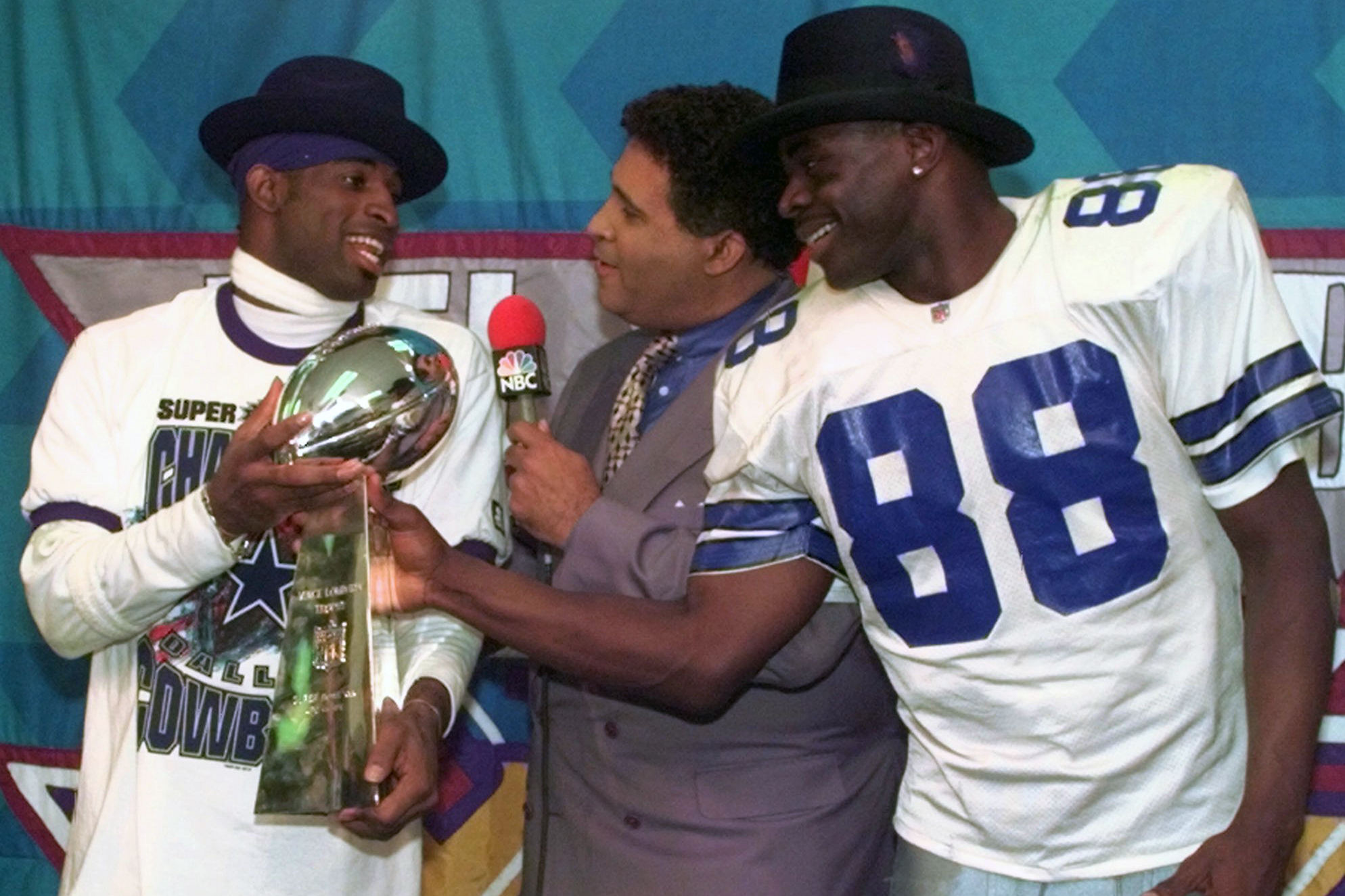 FILE - Dallas Cowboys cornerback Deion Sanders, left, and running back Michael Irvin (88) share the Vince Lombardi trophy as NBC commentator Greg Gumbel interviews the two after Super Bowl XXX in Tempe, Ariz., Sunday, Jan. 28, 1996. (AP Photo/Ron Heflin, File)