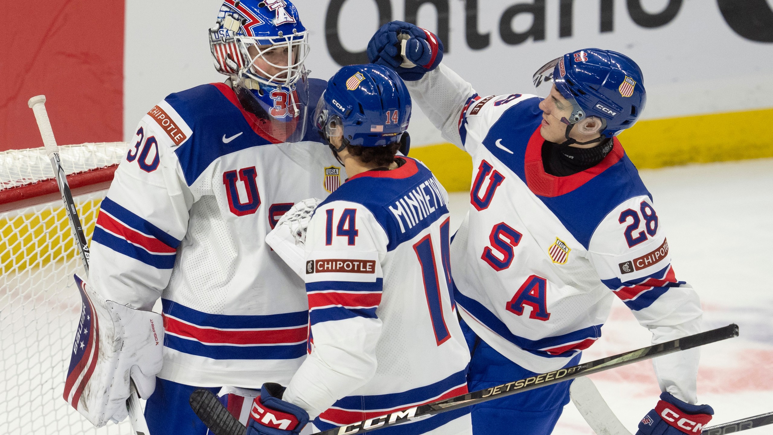 United States defenseman Aram Minnetian (14) and defenseman Zeev Buium (28) congratulate goaltender Hampton Slukynsky after a IIHF World Junior Hockey Championship tournament game against Latvia, Saturday, Dec.28, 2024 in Ottawa, Ontario. (Adrian Wyld/The Canadian Press via AP)